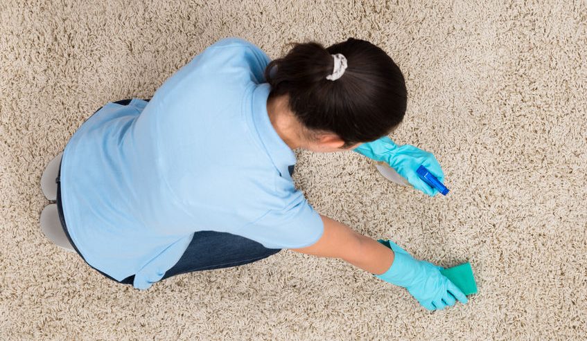 young woman cleaning carpet with detergent spray bottle and sponge